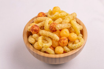 Assorted puff corn snacks in wooden bowl on light background