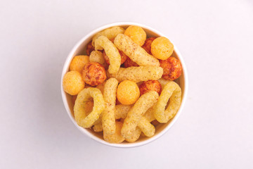 Assorted puff corn snacks in paper cup on light background