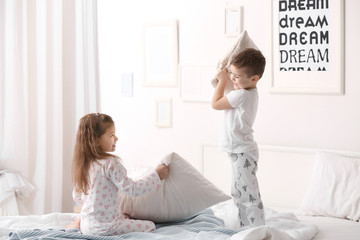 Cute children having pillow fight on bed at home