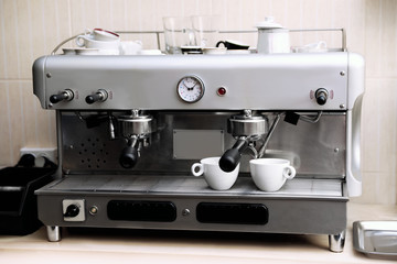 Modern electric coffee machine with portafilters and cups on table indoors