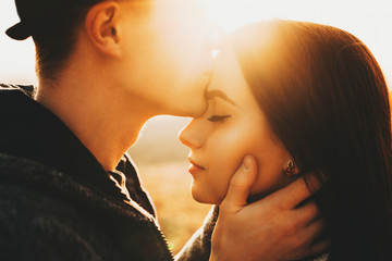 Side view of crop male kissing pretty girlfriend in forehead while spending time in nature on sunny...
