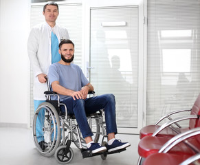 Male doctor taking care of man in wheelchair indoors