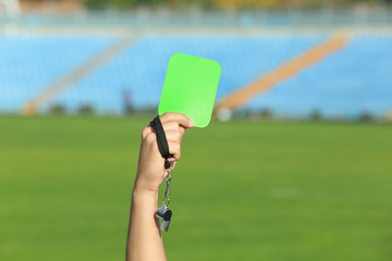 Football referee holding green card and whistle at stadium, closeup