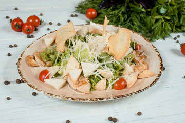 Fresh salad caesar closeup on brown plate on white textured table with cherry tomatoes and chilli and pepper spices and green at background