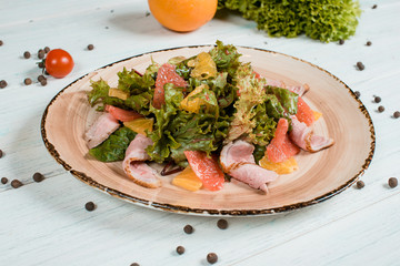 Fresh salad on brown plate on white textured table with cherry tomatoes and chilli and pepper spices and green at background