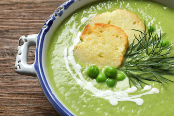 Fresh vegetable detox soup made of green peas with croutons in dish on wooden table, closeup