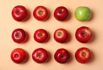 Green apple among red ones on color background, top view. Be different
