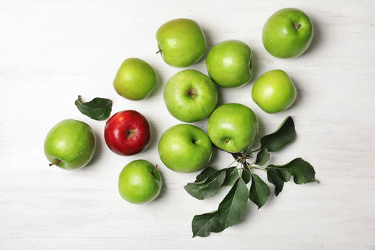 Red apple among green ones on wooden background, top view. Be different