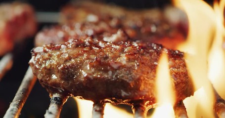 closeup of meat on the grill of a barbeque cooking on a high flame. 