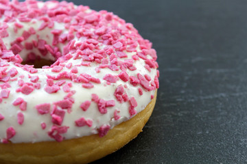 Half Donut with white frosting and pink sprinkles on a black board