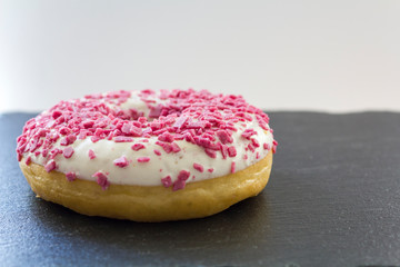 White frosted donut with pink sprinkles on black board