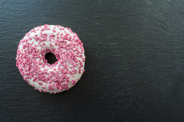 Top view of Glazed donut or Doughnut with pink sprinkles on black board. With copy space