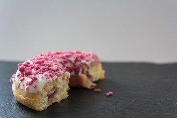 Half Donut with white frosting, pink sprinkles and strawberry filling on black board
