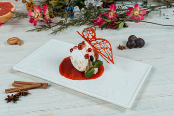white icecream dessert with mint and red sause on white square plate on white table with cinnamon and spices on background