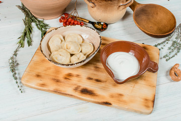 dumplings with cheese and potatoes and sour cream on a wooden board on white tablr traditional russian boiled food