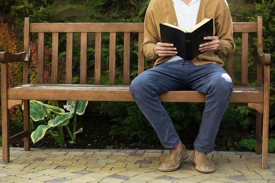 Closeup on a Man Reading a Bible on a Bench