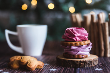 Close up of homemade pink and purple zephyr or marshmallow in powdered sugar with white mug on wooden with abstract bokeh background. Black currant, blueberry marshmallows.