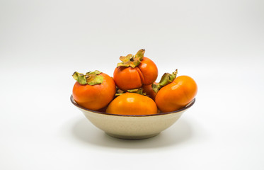 ripe orange persimmons stacked in a bowl isolated on white