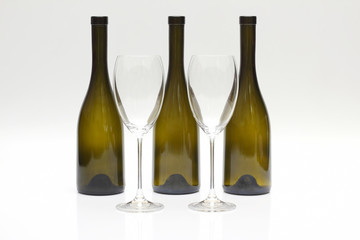 Three empty upturned wine bottles and two glasses on a white background
