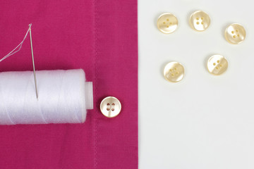 Needle with white threads and sewn pearl buttons on the shirt