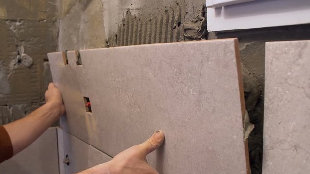 Gluing tiles on the wall. Laying tiles on the wall.  Worker installing big ceramic tiles on the walls