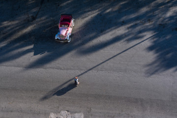 Un hombre agachado toma fotos a un auto antiguo en una calle de la Habana vieja.