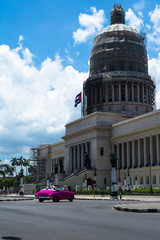 Un carro antiguo de color rosado está pasando cerca del Capitolio de la Habana.
