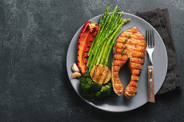 Tasty and healthy salmon steak with asparagus, broccoli and red pepper on a gray plate. Diet food...