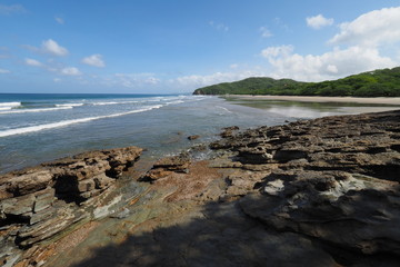Fototapeta na wymiar Playa El Coco, Nicaragua, on a sunny summer day showing its beach, rocks, vegetation and cloudscape.