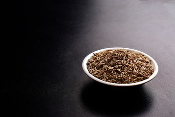 cumin seeds in ceramic bowl, text space , black background