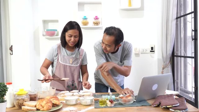 Asian men and women cooking with receipt on laptop computer in the kitchen      