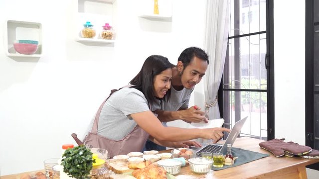 Asian men and women cooking with receipt on laptop computer in the kitchen      