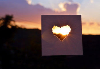 Sunset behind a heart shaped paper