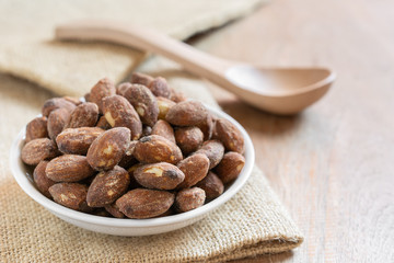 close up of salt roasted almond in a small ceramic dish on wooden table. healthy snack concept.