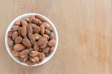 top view of salt roasted almond in a small ceramic dish on wooden table with copy space. healthy snack concept.