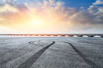 Asphalt road pavement and dramatic sky with bridge at sunset