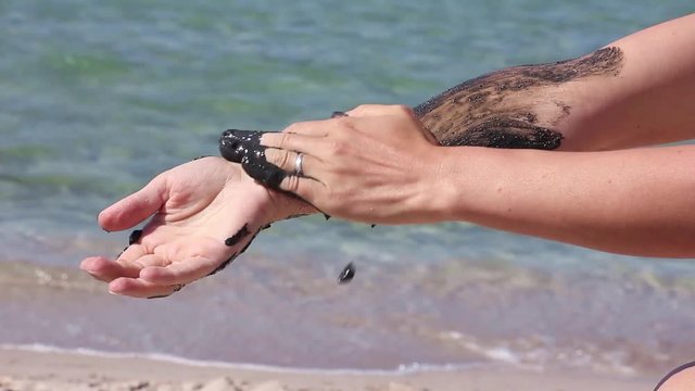 the girl continues to covers her hand and the palm with therapeutic mud, on the background of sea beach