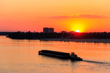 Tugboat pushing a heavy long barge on the river Dnieper at sunset