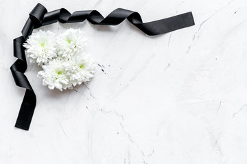Funeral symbols. White flower near black ribbon on white stone background top view copy space