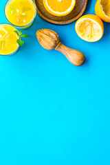 Make orange juice. Juice in glass near half cut oranges and jucier on blue background top view copy space