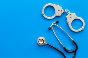 Medical lawsuit. Arrest for medical crime concept. Handcuff near stethoscope on blue background top...