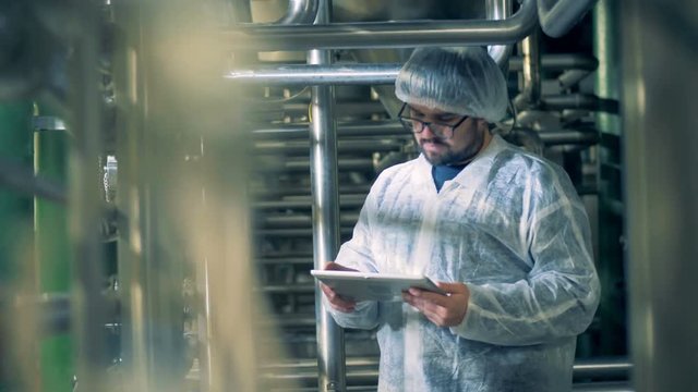 Distillery facility with a male technician observing it and working with a tablet
