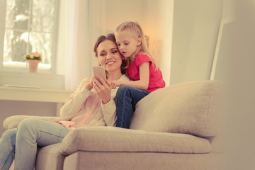 Fototapeta premium Joyful nice woman showing her smartphone to the daughter