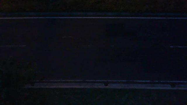 Top shot of a patched asphalt road at night and some cars passing by with their lights on