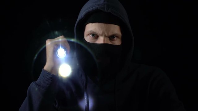 Lawbreaker in balaclava mask flashing torch, searching for important information