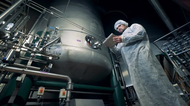 Male worker is controlling functioning process of brewing equipment