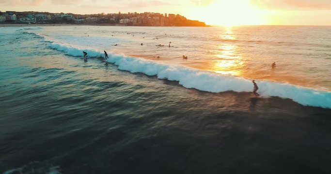 Tracking aerial shot of a surfer catching a wave at Bondi Beach during sunrise.