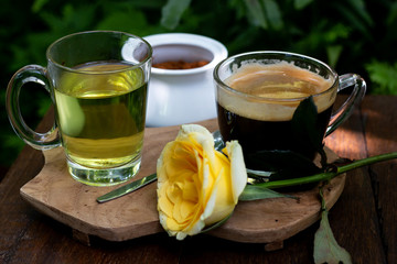 Coffee and tea are on the wooden table in green garden
