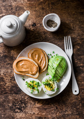 Peanut butter toasts, boiled egg with micro greens, avocado - healthy breakfast or snack on a wooden background, top view