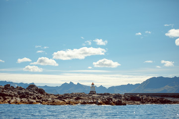 Image of lighthouse on sea against background of rocks and cloudy sky